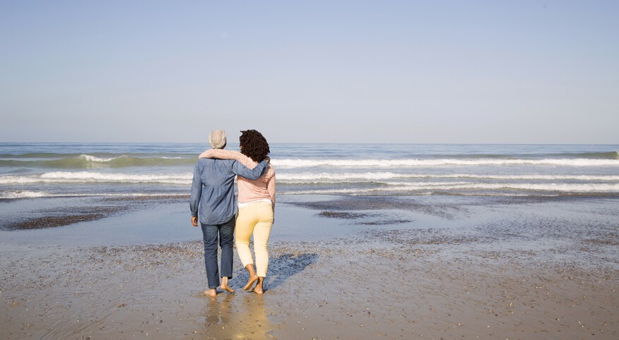 Black women hugging and walking on beach