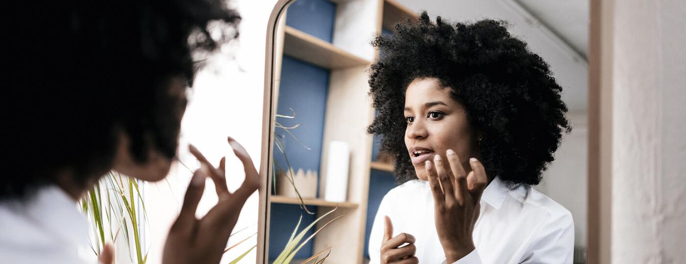 Woman looking in mirror at a dark spot on her face.