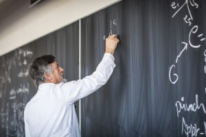 Senior chemistry professor writing on the board while having a c