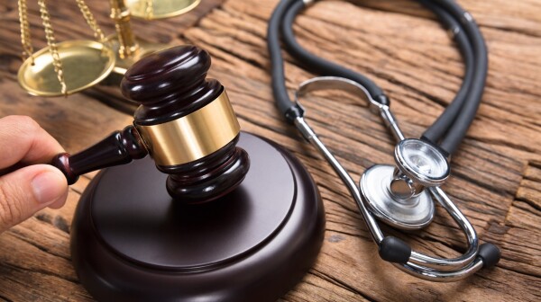 Judge's Hand Hitting Mallet By Stethoscope And Justice Scale
