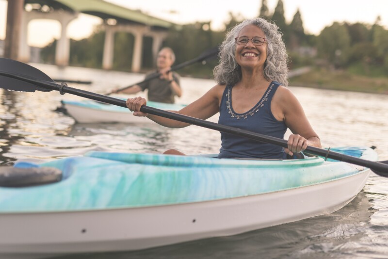 An ethnic senior woman smiles while kayaking with her husband