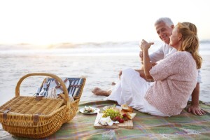 Happy senior couple seated on the beach and enjoying a picnic