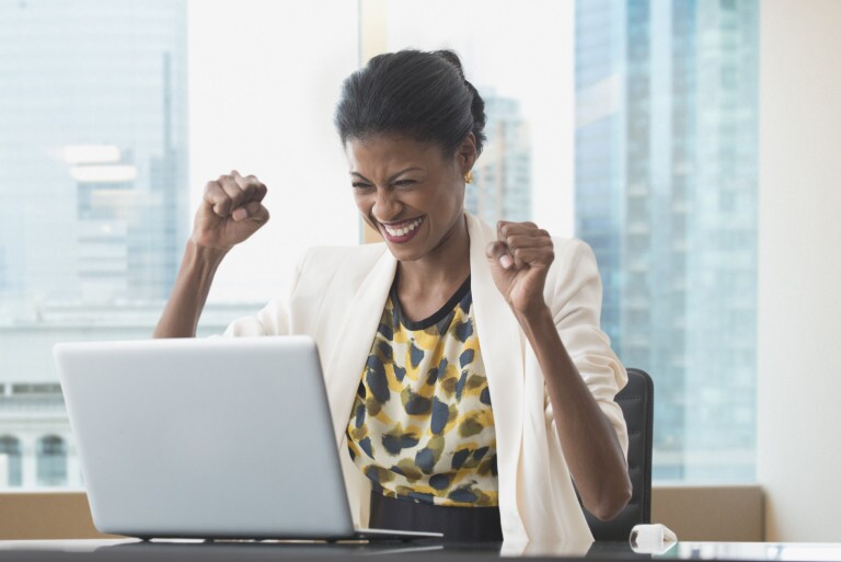 Mixed race businesswoman cheering at laptop at office desk