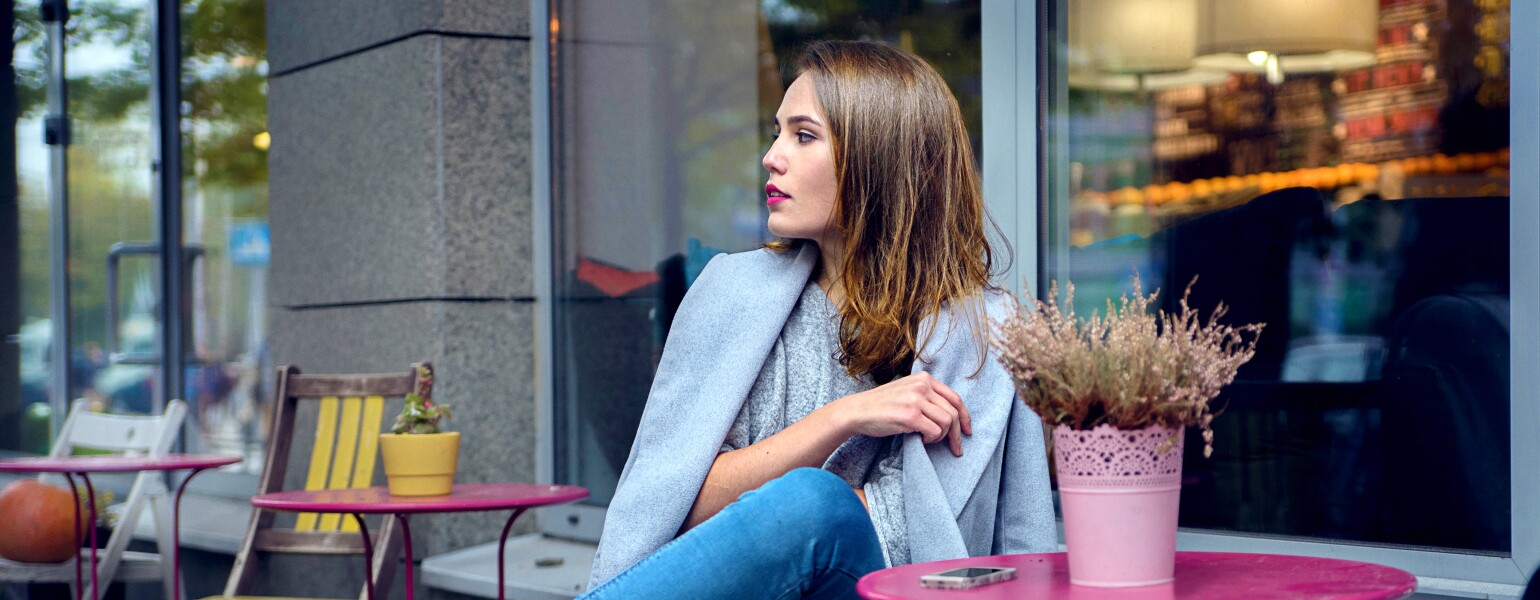 A woman in grey coat and blue jeans is waiting for someone at the cafe