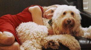 Woman in red dress hugging her dog on the couch