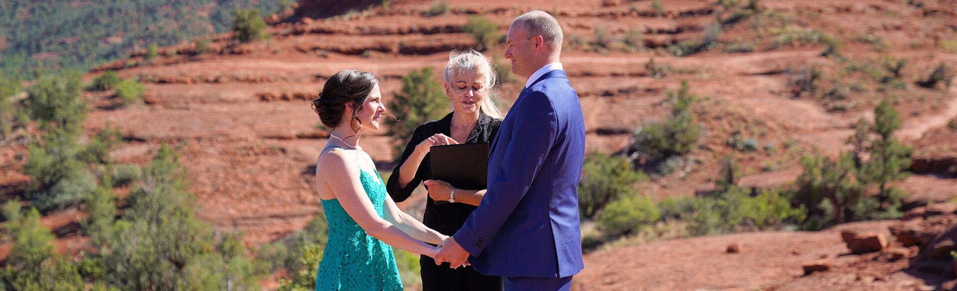 A couple with their officiator standing on red rocks for their private wedding ceremony