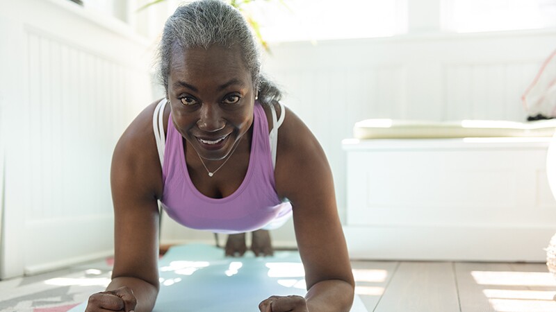 A smiling woman doing a plank on a yoga mat