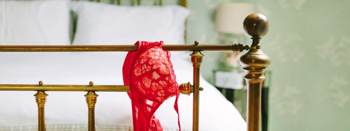 end of bed post with red bra hanging off the edge