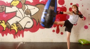 young teenager girl in a boxing gym kicking a large punching bag