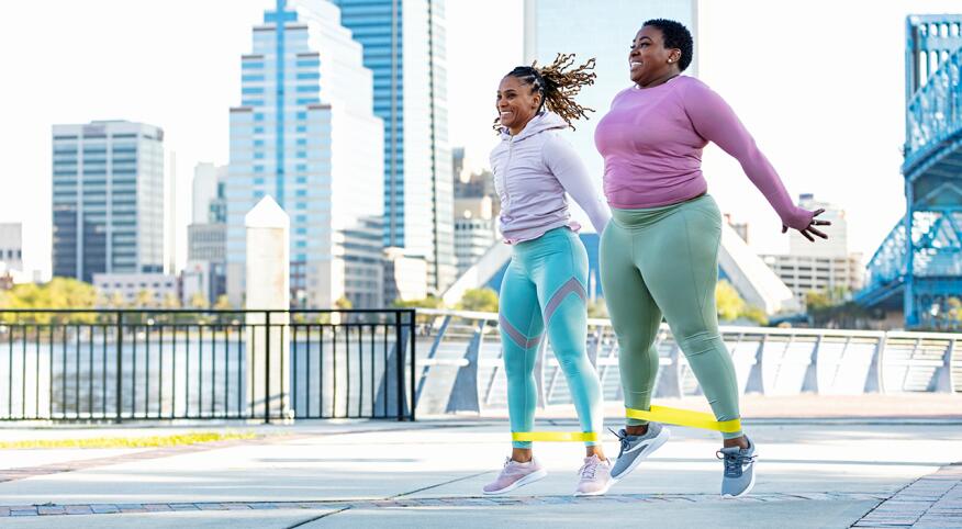 Two women in front of a cityscape doing jumping jacks