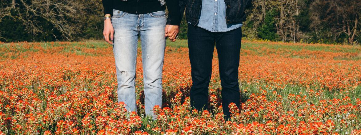 Couple standing hand in hand in a field of wildflowers.