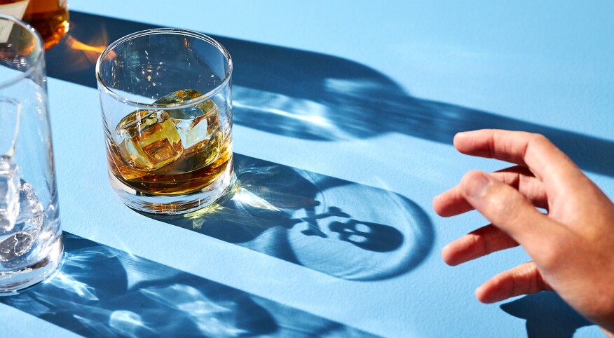 Hand reaching out to alcohol drink with shadow of skull and cross bones