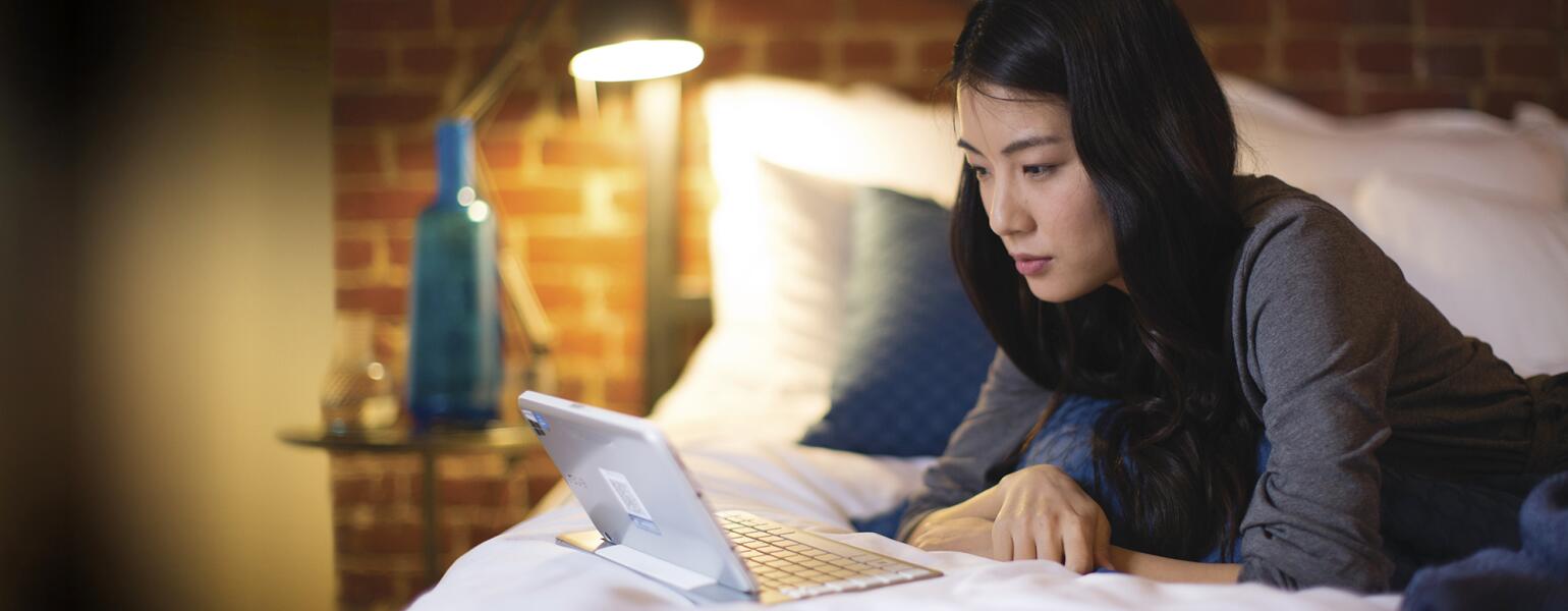 Woman lying on her bed looking at Google on her computer