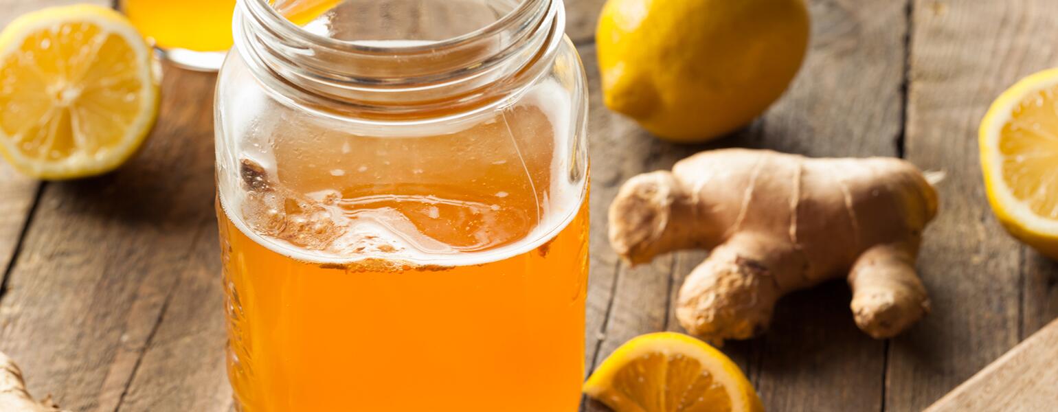 Kombucha in a mason jar surrounded by ginger lemon and oranges