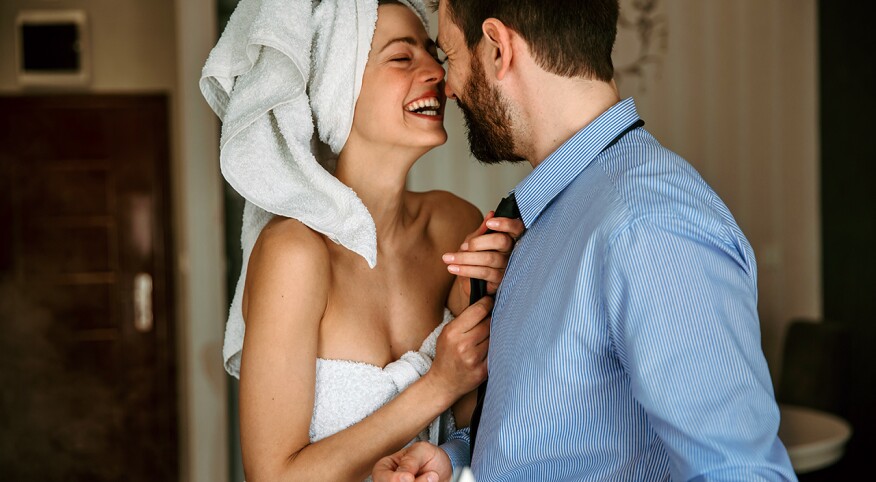 Couple standing in bedroom with woman pulling at man's tie