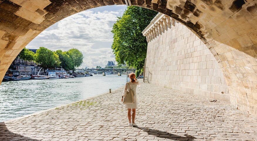 Beautiful middle aged woman taking a photo with smart phone under the arch by the river in Paris