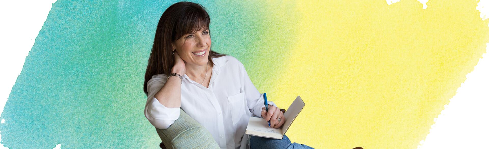 Jean Chatzky sitting in a chair writing in a notebook with water color background