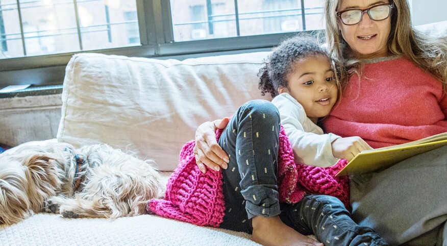 mom reading to her adopted daughter on a couch next to a dog