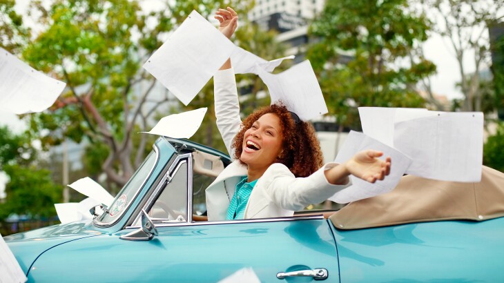 Happy woman in convertible throwing documents into the air