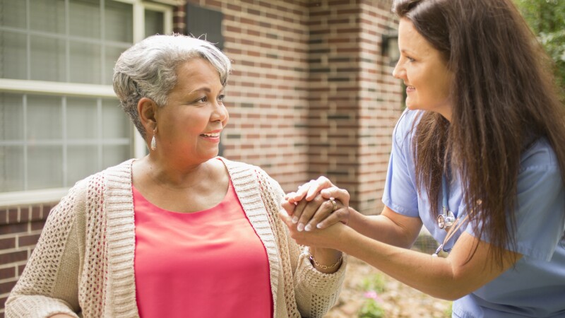 Senior adult with home healthcare nurse, caregiver outdoors. Home, wheelchair.