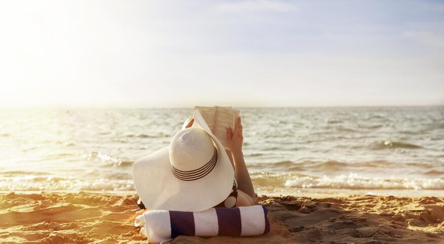 woman laying on towel reading on beach in the sun