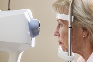 Senior woman (60s) at ophthalmologist's office for eye exam, looking into retina scanner.