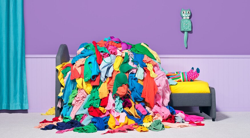 A person under a pile of clothes in the bedroom