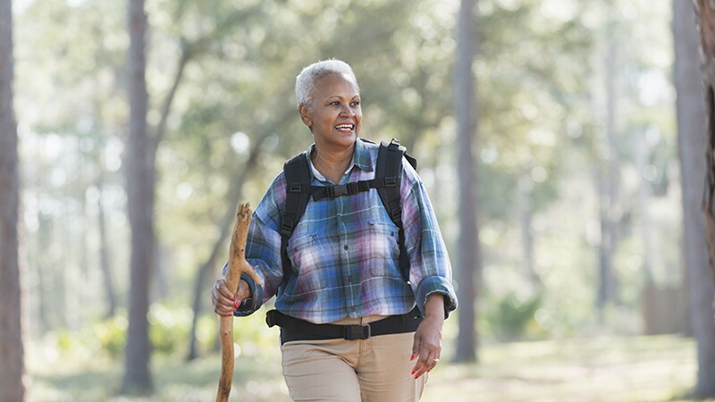 A woman carrying a backpack and walking stick as she hikes through the woods