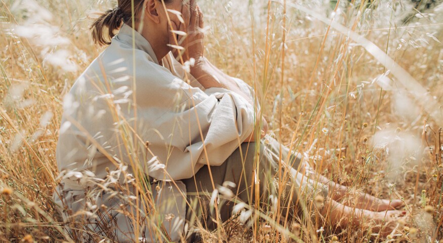 woman in a wheat field with hands over face