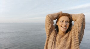 happy woman in her 40s by the water in a sweater