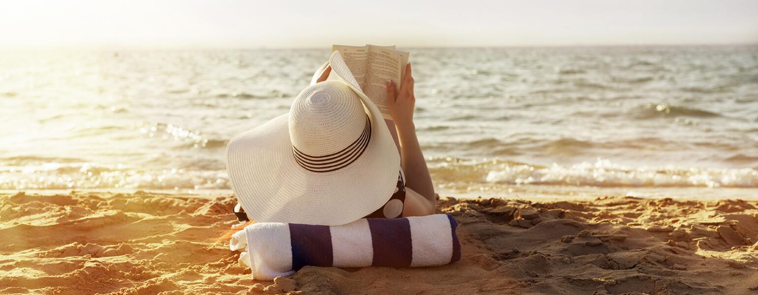 woman laying on towel reading on beach in the sun