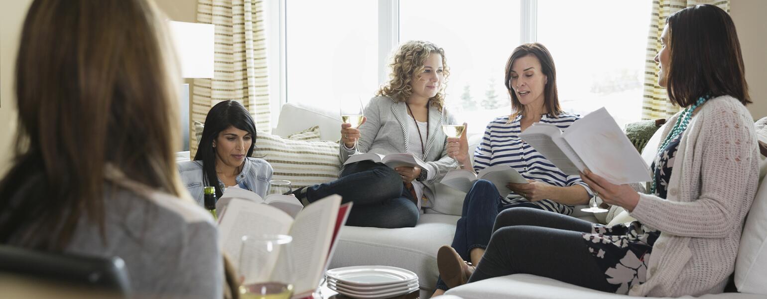 Mature female friends with wine glasses and books at a book club