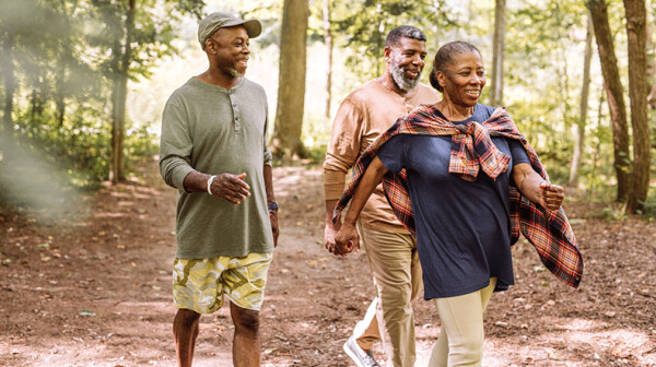 One Black woman and two Black men walk in a forest