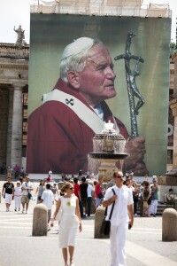 Tourists walking in St. Peter's Square in front of the manifest with the face of Pope John Paul II