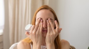 woman putting eye cream over her eyes at home
