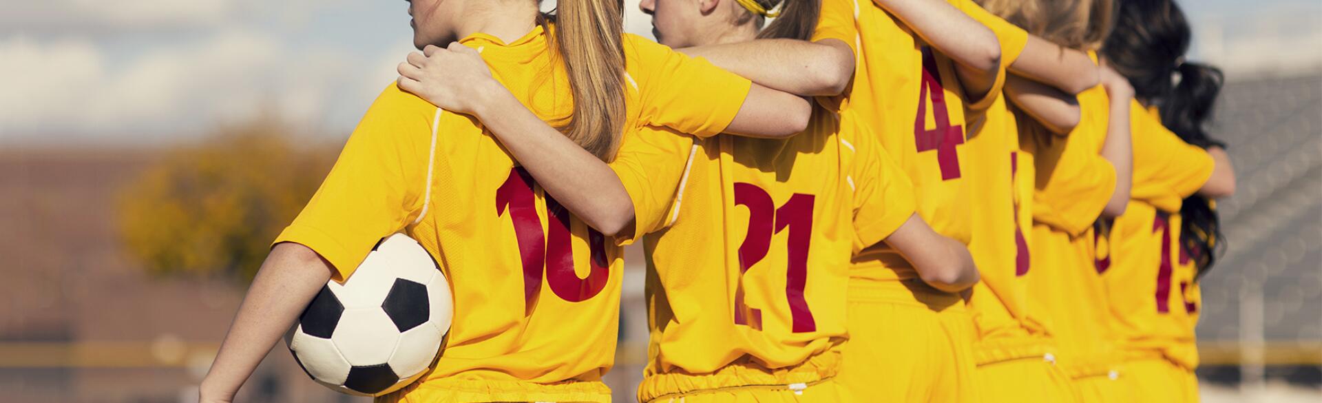 Young girls playing soccer standing on the sidelines arm and arm before the game