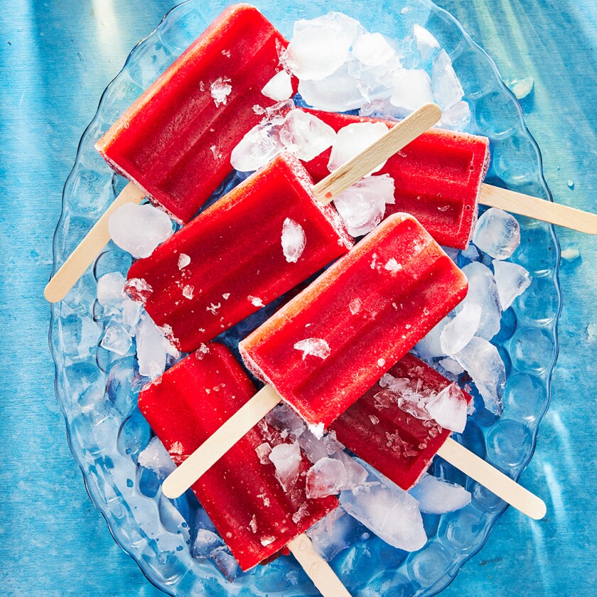 Brigth red strawberry popsicles surrounded by ice on a bright blue background
