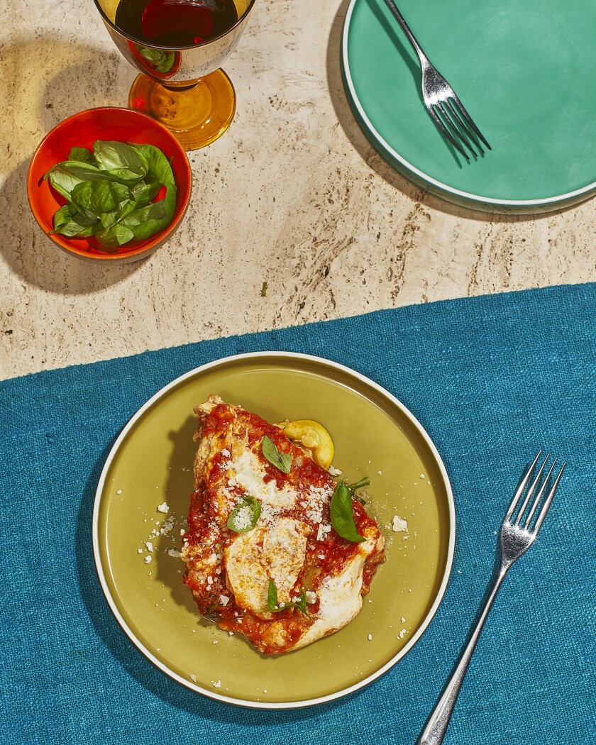 Lasagne topped with parmesan cheese and basil on a blue table mat with a side of red wine