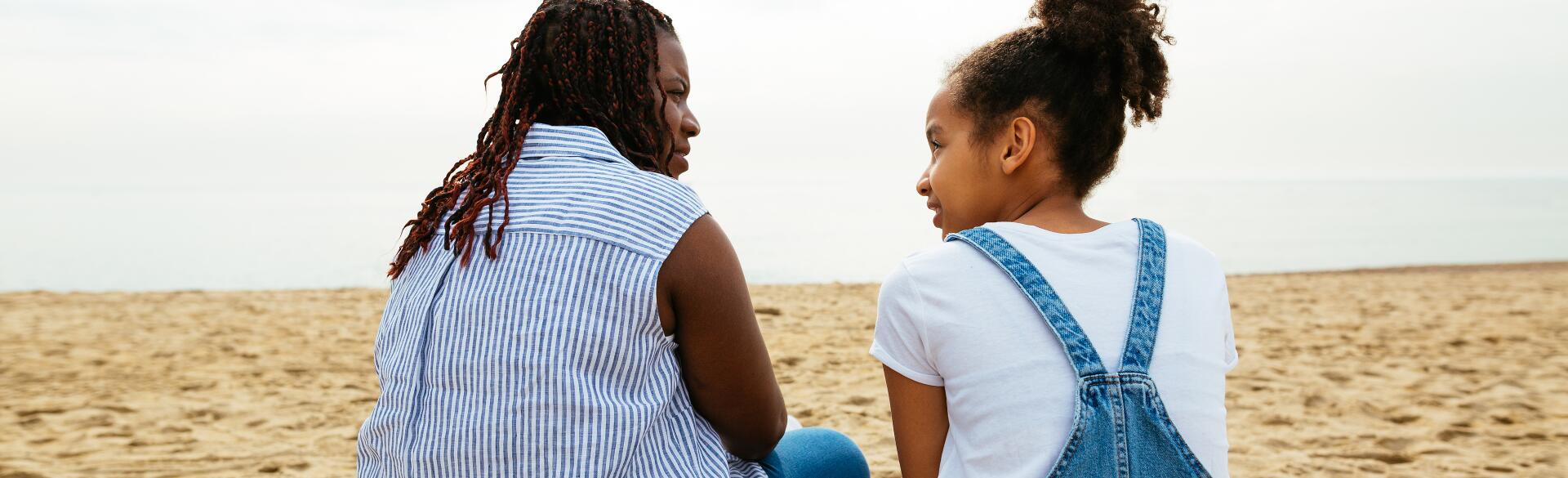 A stepmother sits with her stepdaughter on the beach.