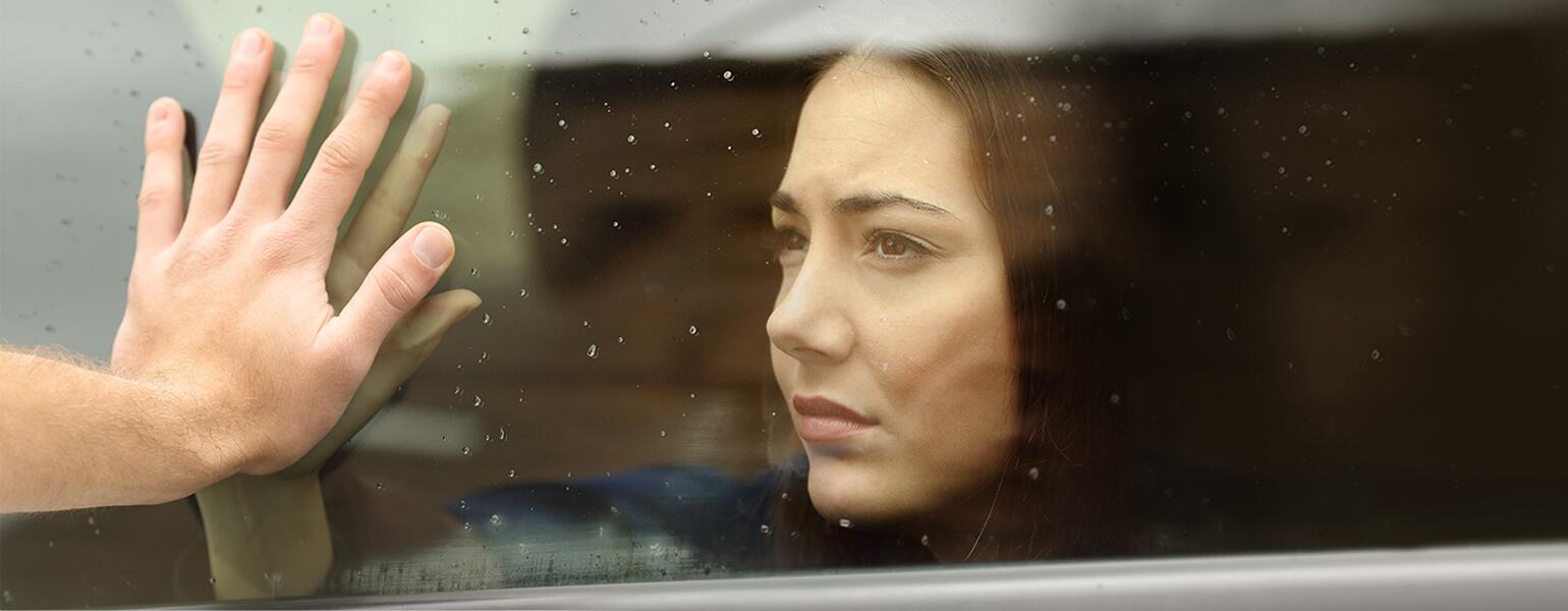 A woman presses her face and hand up against a piece of glass against a parent's hand on the other side.