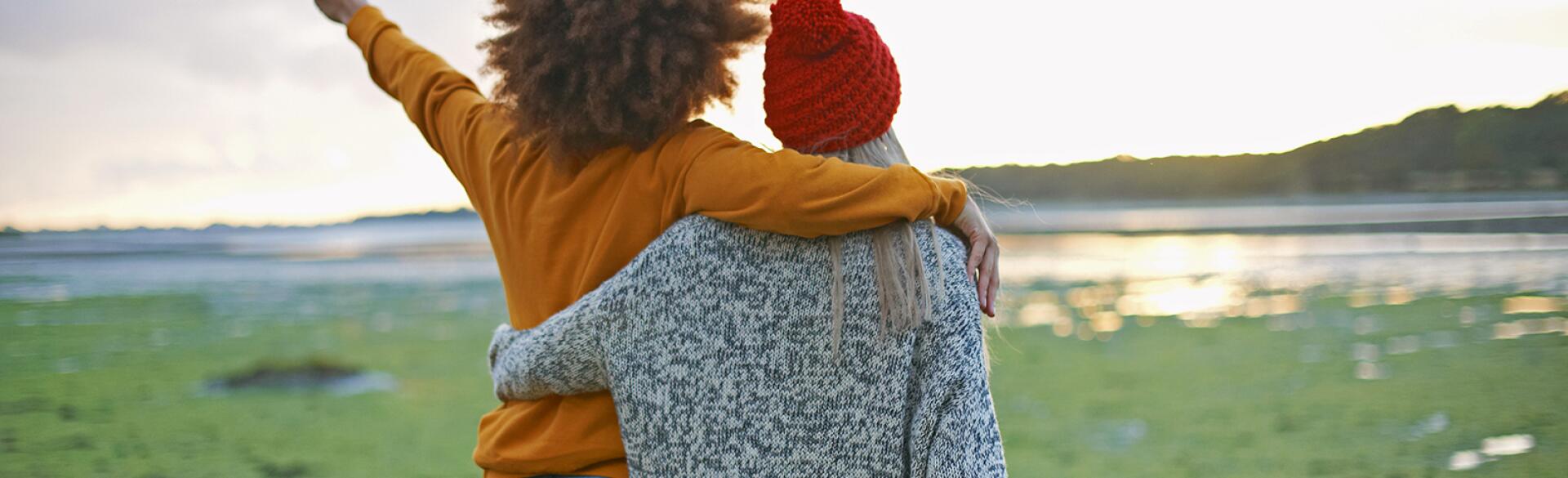 Rear view of two young forever friends by sea pointing at sunset