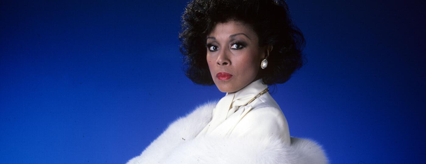Diahann Carroll on blue background in white suit from TV show Dynasty