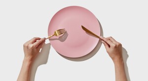 An image of a person holding a fork and knife over an empty plate.