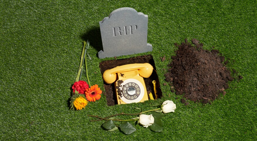 Grave yard scene with a RIP tombstone and a classic rotary dial phone in the ground surrounded by flowers