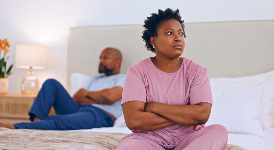 Black couple with arms crossed sitting apart from each other on their bed