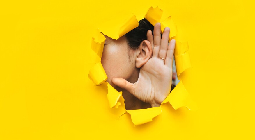 Close-up of a woman's ear and hand through a torn hole in the paper. Yellow background, copy space. The concept of hearing loss