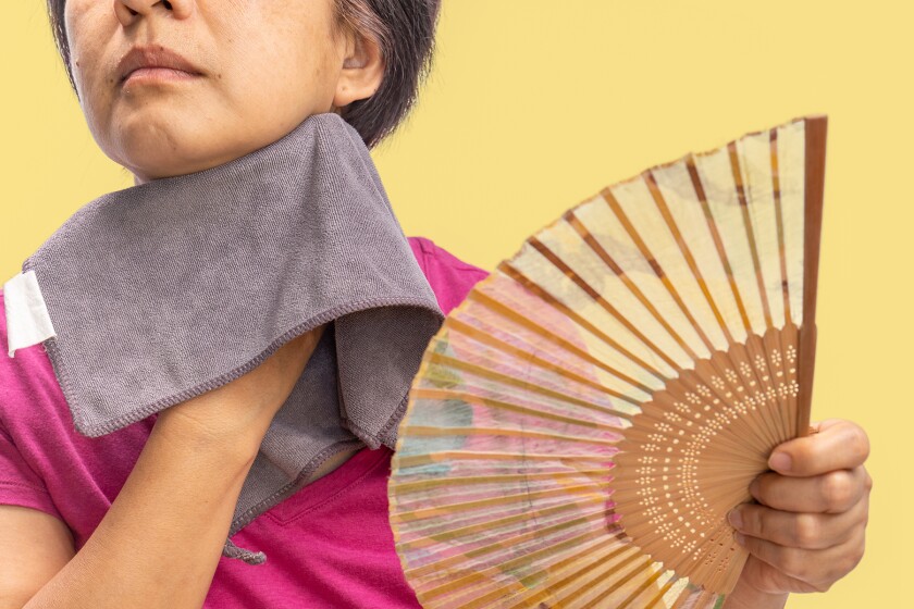 Middle aged woman feel hot flashes or overheated , symptoms of menopause, using fan and towel