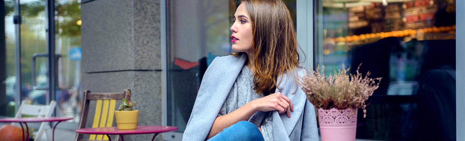 A woman in grey coat and blue jeans is waiting for someone at the cafe