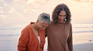Senior friends, beach and smile together on vacation, holiday or adventure by ocean while walking. Elderly women, sea and conversation on happy walk on sand to laugh, relax or bonding for hug outdoor