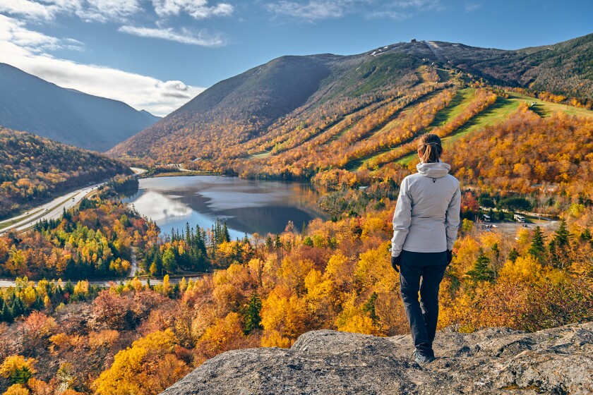 Woman hiking at Artist's Bluff in autumn. View of Echo Lake. Fall colours in Franconia Notch State Park. White Mountain National Forest, New Hampshire, USA
